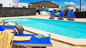 Ein Poolbereich mit blauen Liegestühlen, einer Steinmauer und einem Berg im Hintergrund.