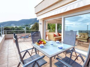 A balcony with a table set for two, chairs, a sofa, and a glass door leading to an outdoor seating area. - Apartment Fane by Interhome (Llançà)