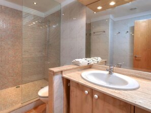 A modern bathroom with a glass shower enclosure, a white sink, and a wooden vanity. - Apartment Fane by Interhome (Llançà)