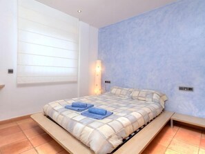 Camera da letto con un letto, un comodino, una lampada a parete e una finestra con persiane.