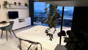 A modern hotel room with a bed, a TV, a dining area, and a balcony with plants.