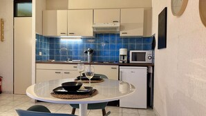 A modern kitchen with a round dining table, two chairs, a microwave, a coffee maker, and a small refrigerator.