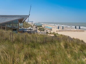 Un hôtel en bord de mer au design moderne, doté d’une façade en verre et d’une terrasse offrant une vue sur la plage.