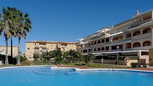 Une piscine de forme circulaire, entourée de palmiers et bordée d’un immeuble à plusieurs étages doté de balcons.