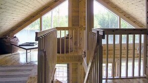 Una habitación de ático con techo inclinado, ventanas amplias y una escalera.