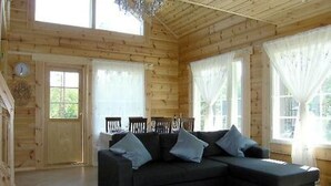 Interior de una cabaña de madera con un sofá de color oscuro, dos sillones y una mesa de comedor.