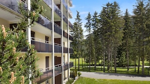 A multi-story building with balconies, surrounded by a well-maintained lawn and tall trees. - Allod Park Haus C 106 by Interhome (Davos)