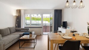 A modern living room with a sofa, coffee table, and dining table. There is a TV and a plant on the table. - Allod Park Haus C 106 by Interhome (Davos)