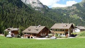 Un chalet de montagne composé de plusieurs bâtiments en bois, une voiture et une grande montagne en arrière-plan.