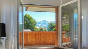 Habitación con puerta de vidrio corredera que da a un balcón con valla de madera y vistas a la montaña.