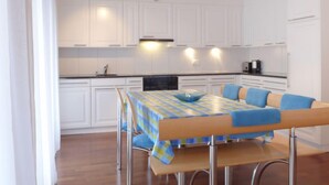 Una cocina moderna con armarios blancos, una mesa de comedor con mantel a cuadros azul y amarillo, y un horno empotrado.