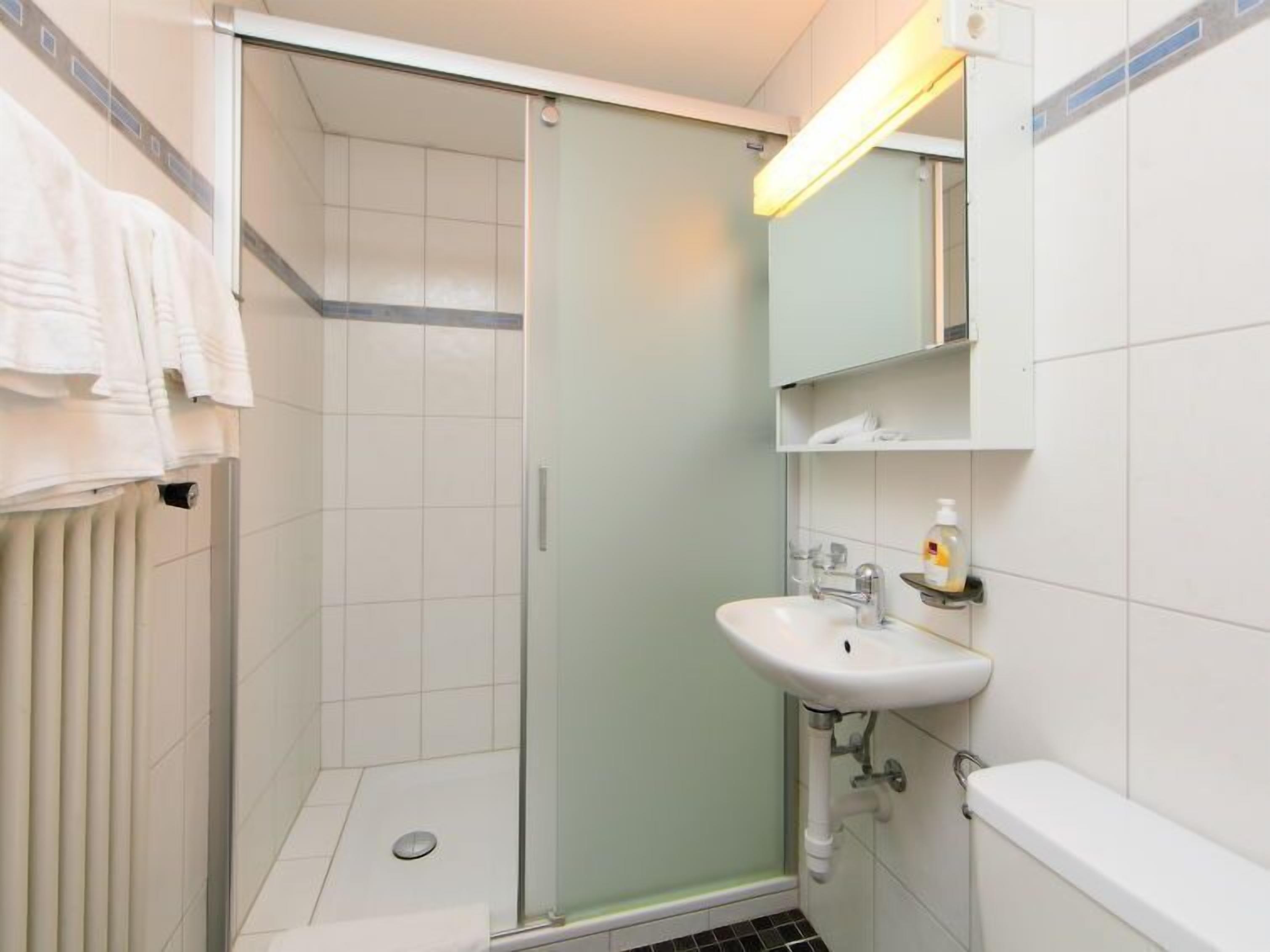 Ein modernes Badezimmer mit einer gläsernen Duschkabine, einem weißen Waschbecken und einem Spiegel darüber.