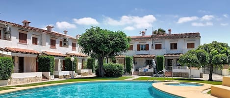 A swimming pool surrounded by a courtyard with white buildings and red-tiled roofs.