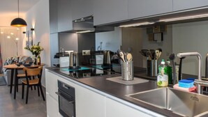 Een moderne keuken met een centraal eiland, roestvrijstalen apparatuur en een eethoek met een tafel en stoelen.
