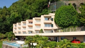 Een hotel met meerdere verdiepingen, balkons, een zwembad en weelderige begroeiing.