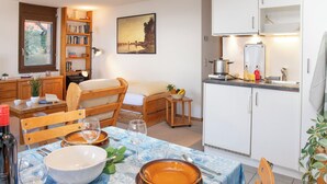 A compact living space with a dining area, a kitchenette, a bed, and a bookshelf. - Primula Apt. B by Interhome (Wengen)