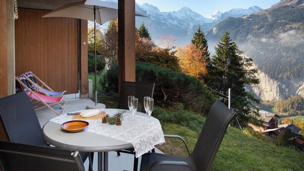 A table set outdoors with a mountain view, including a chair with a pink cushion and a wooden bowl. - Primula Apt. B by Interhome (Wengen)