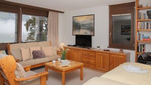 A cozy living room with a sofa, coffee table, and a TV. There's a bookshelf with books and a painting on the wall. - Primula Apt. B by Interhome (Wengen)