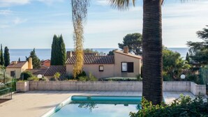 En swimmingpool med utsikt över havet, omgiven av palmer och hus.