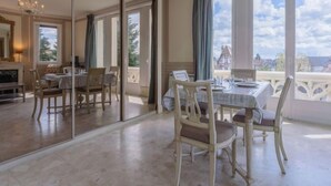 A dining area with a table set for four, large windows with curtains, and a view of the cityscape. - Marie Antoinette by Interhome (Cabourg)