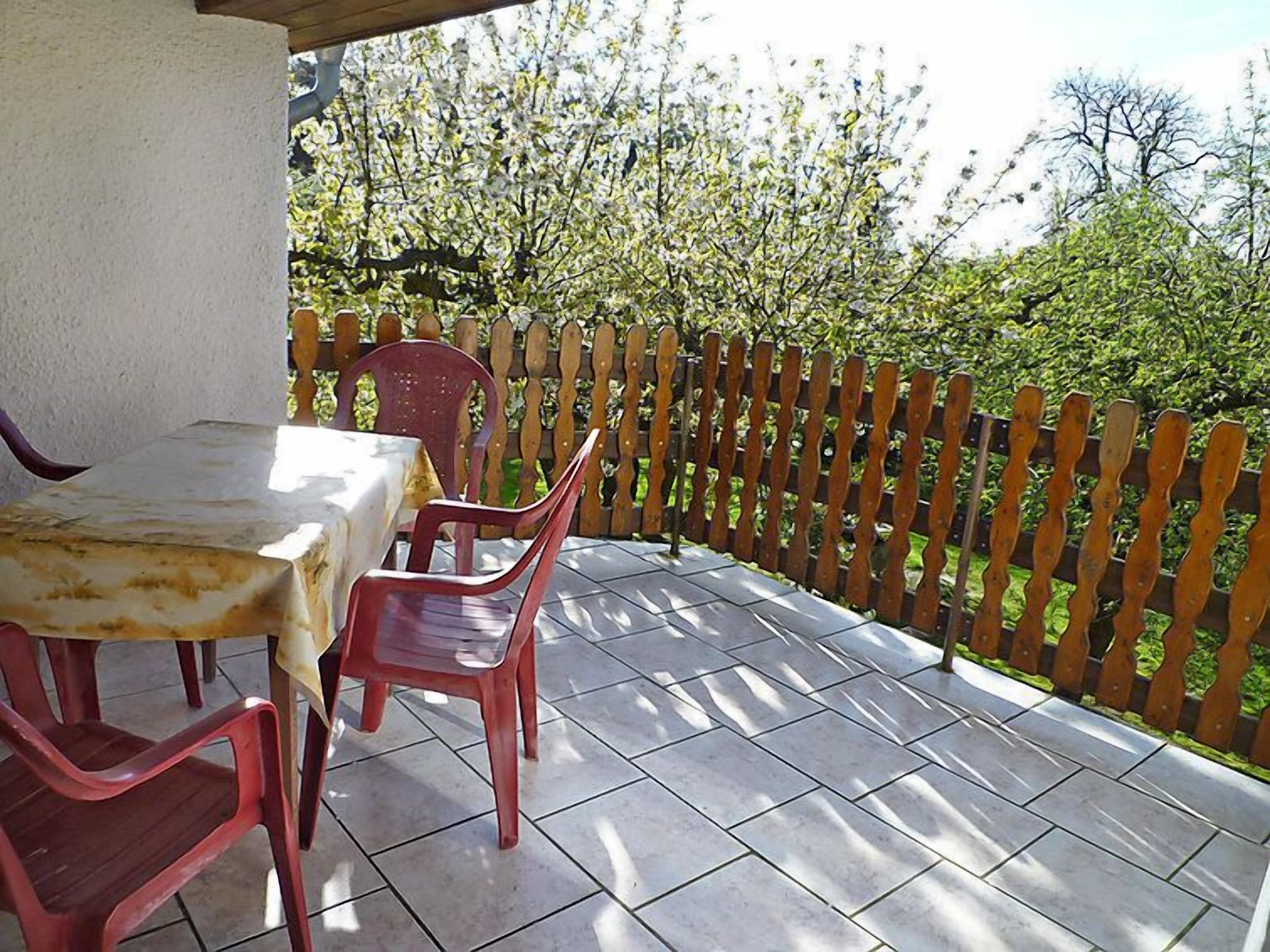 A patio with a table and chairs, a wooden fence, and a view of trees.