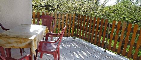 A patio with a table and chairs, a wooden fence, and a view of trees.