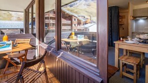 Ein gemütliches Zimmer mit Holztisch und -stühlen, ein großes Fenster mit Blick auf einen Berg und einer Küchenzeile mit Grundausstattung.