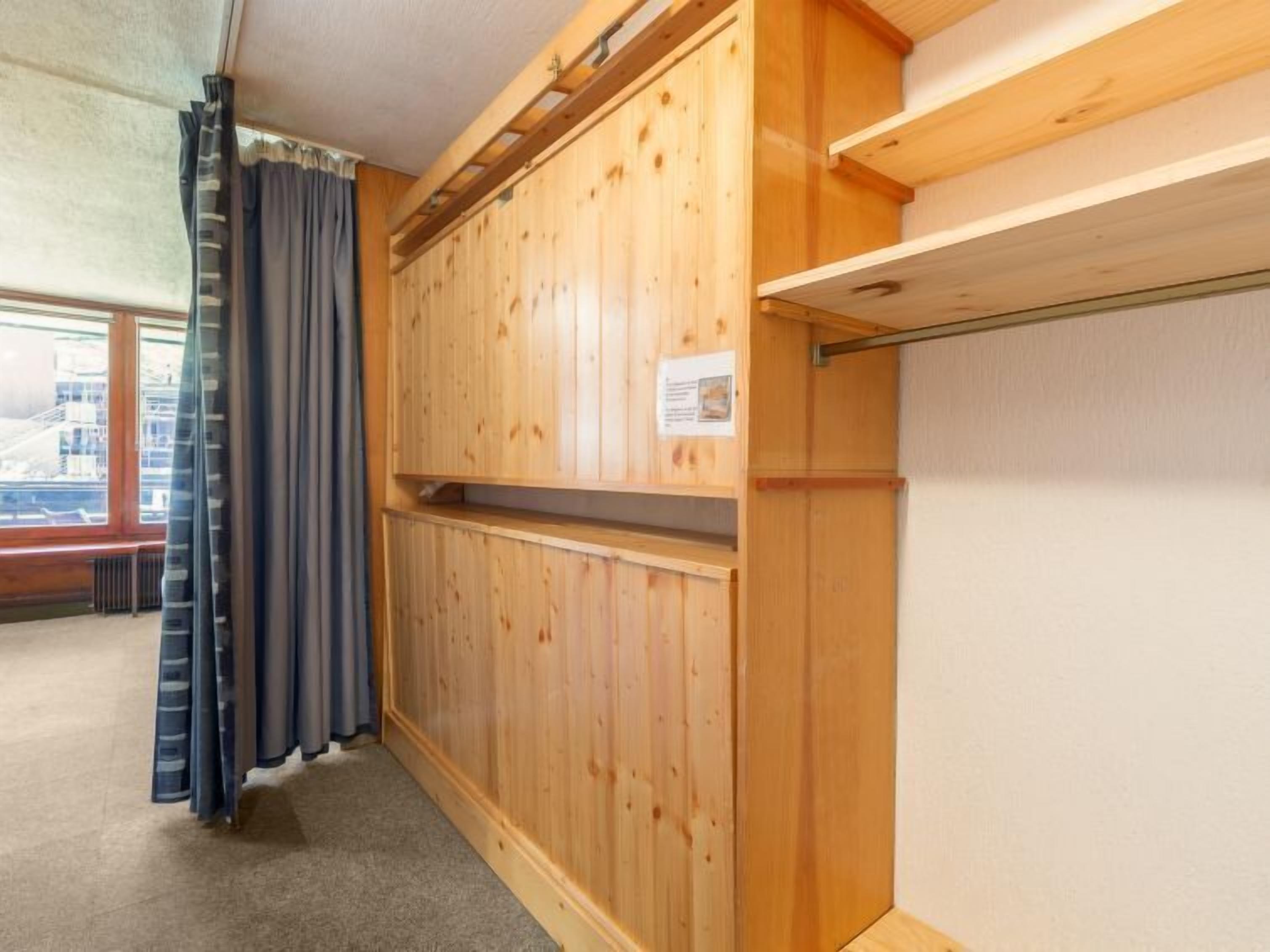 A room with wooden panel walls, a window with curtains, and a radiator on the floor.
