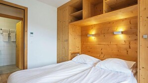 Un dormitorio con cabecera de madera, cama con sábanas blancas y dos lámparas de pared.