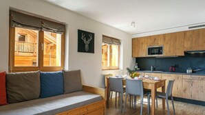 Una habitación acogedora con un sofá de madera, una mesa de comedor con sillas, una zona de cocina con armarios de madera y un microondas, y una ventana con vista a una estructura de madera exterior.