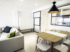 Uma sala de estar moderna com um sofá, uma mesa de jantar com cadeiras e uma luminária pendente.