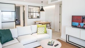 Un salon moderne avec un canapé blanc, une table basse ronde et un téléviseur posé sur un meuble blanc.