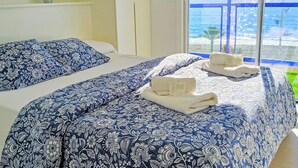 Une chambre d’hôtel avec deux lits, chacun agrémenté d’une literie à motifs floraux bleus et de coussins blancs. On trouve des serviettes sur les lits et une petite plante en pot sur une étagère.