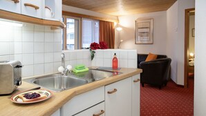 Cocina pequeña con un lavamanos, un tostador y un plato de comida. Se ve una ventana con cortinas y un cuadro en la pared.