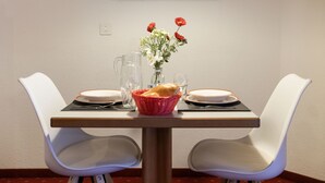 Una mesa de comedor con dos sillas blancas, un florero con flores, una jofaina y una cesta de pan.