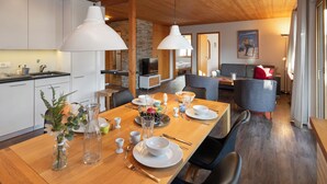 A modern kitchen with white cabinets, a dining table set for four, and a cozy living area with a sofa and a TV. - Chalet Bienli Mitte by Interhome (Grindelwald)