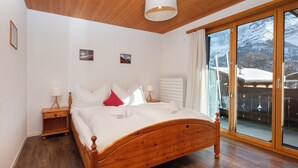 A wooden bed in a room with a large window, a nightstand, and a wall-mounted heater. - Chalet Bienli Mitte by Interhome (Grindelwald)