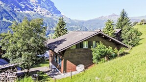 A wooden cabin with a sloped roof, surrounded by trees and a mountain backdrop. - Chalet Bienli Mitte by Interhome (Grindelwald)