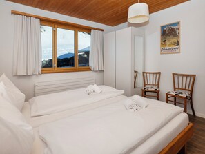 Ein Schlafzimmer mit zwei Betten, einem Vorhangfenster, einem Spiegel und einem Bild an der Wand.