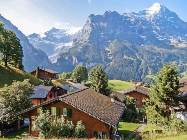 Ein Bergdorf mit traditionellen Holzhäusern, freiem Blick auf die umliegenden Berggipfel und einer üppigen grünen Landschaft.