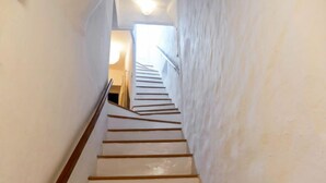 Een smalle trap met witte muren en houten leuningen die leidt naar een lichte kamer aan de bovenkant.