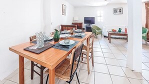 Een eethoek met een houten tafel voor vier personen, omringd door stoelen. Een televisie is aan de muur bevestigd, en er is een raam dat zorgt voor natuurlijk licht.