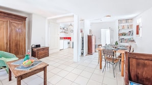 Een ruime woonkamer met een houten eettafel, een keuken op de achtergrond en een boekenkast vol boeken.