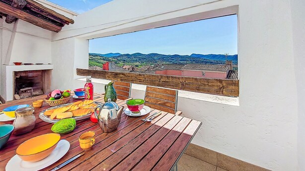 Een terras met een gedekte tafel, uitzicht op het landschap en een witte muur met een raam.
