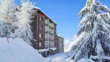 Un immeuble à plusieurs étages doté de balcons, entouré d’arbres couverts de neige et surplombant un ciel bleu clair.