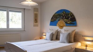 A bedroom with a bed, bedside lamps, a window, and a wall-mounted painting.