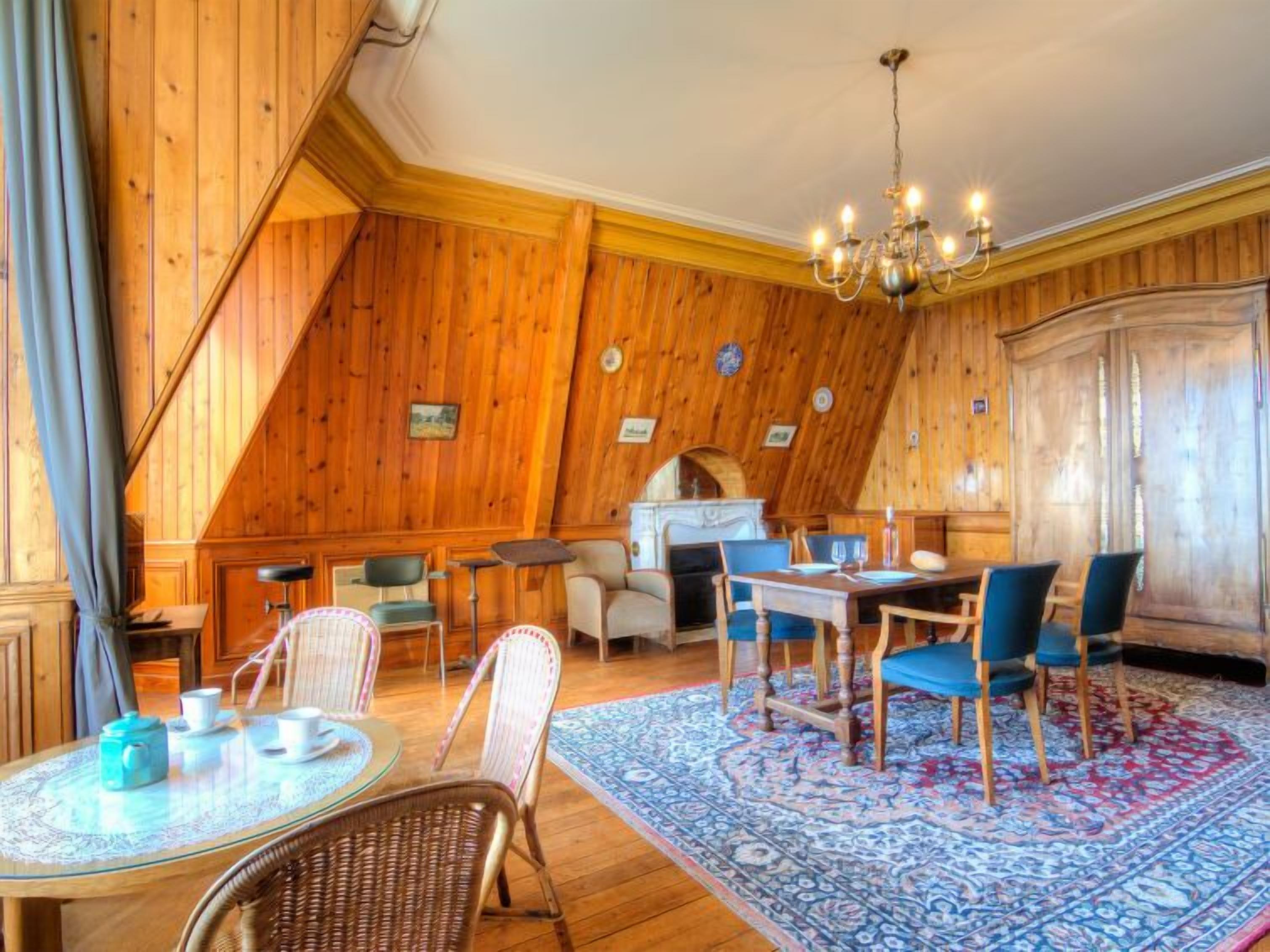 Une pièce chaleureuse aux murs en bois, avec une table à manger, des chaises et un lustre.