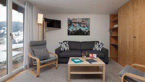 A modern living room with a sofa, armchair, coffee table, and a flat-screen TV. - Chalet Jolimont by Interhome (Grindelwald)