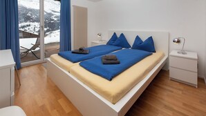 A modern bedroom with a large bed, a bedside table, a chair, and a view of a snowy landscape. - Chalet Jolimont by Interhome (Grindelwald)