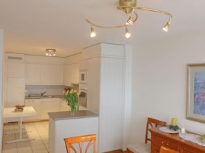 A compact kitchen with white cabinets, a dining area with a wooden table and chairs, and a ceiling light fixture.